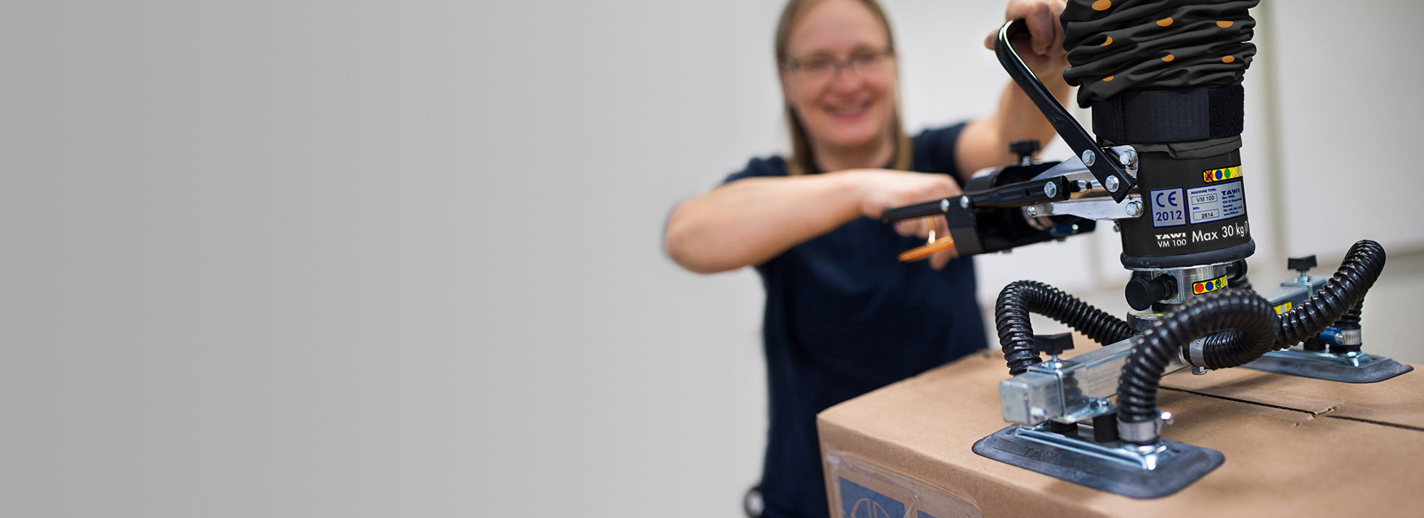 Mujer feliz levantando caja sin esfuerzo con manipulador multifuncional de tawi